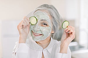 Beauty, skin care, antiwrinkle treatment concept. Headshot of beautiful Caucasian senior woman, holding cucumber piece photo