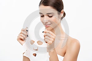 Beauty Skin Care Concept - Beautiful Caucasian Woman applying paper sheet mask on her face white background.