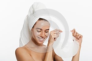 Beauty Skin Care Concept - Beautiful Caucasian Woman applying paper sheet mask on her face white background.