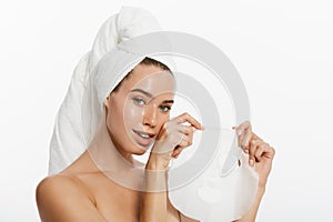 Beauty Skin Care Concept - Beautiful Caucasian Woman applying paper sheet mask on her face white background.