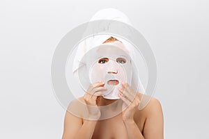 Beauty Skin Care Concept - Beautiful Caucasian Woman applying paper sheet mask on her face white background.