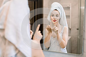 Beauty and skin care concept, spa at home. Attractive young woman wrapped in towel, applying moisturizing lifting facial