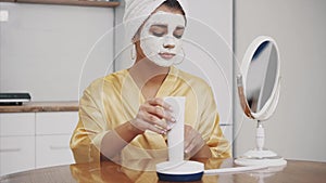 Beauty, skin care and people`s concept. Smiling young woman. Apply mask to the face and while looking at the mirror and