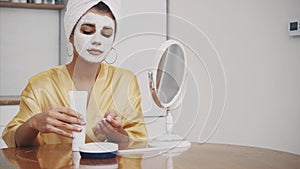 Beauty, skin care and people`s concept. Smiling young woman. Apply mask to the face and while looking at the mirror and