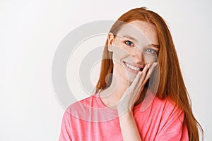 Beauty and skincare. Close-up of young redhead woman with freckles and blue eyes touching clean, no make-up skin and