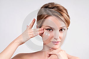 Beauty and skincare concept. Young woman applying moisturizer on face.