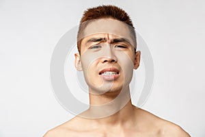 Beauty, skincare and men health concept. Headshot ot troubled and nervous young asian man with naked torso, grimacing