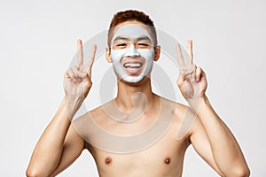 Beauty, skincare and spa concept. Cheerful young asian guy with naked torso applied skin routine cosmetics, facial mask