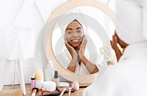 Beauty skincare. Young beautiful black woman touching her face near mirror