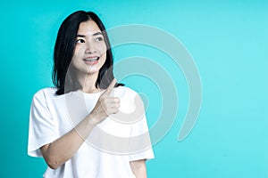 Beauty smiling brunette Asian woman pointing away and smiling and looking at the camera over color background