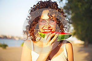 Beauty smiling curly woman is wearing pink sunglasses and eating watermelon