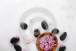 Beauty, spa background with black massage stone and flowers in bowl on white table top view. Relaxation and wellness concept.
