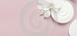 Beauty Spa concept. Opened plastic container with cream and White Phalaenopsis orchid flowers on pink background Flat lay top view