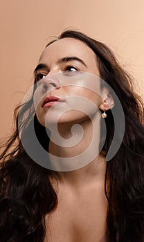 Beauty studio portrait of a beautiful young woman with long dark hair and natural glowing skin on a beige background.