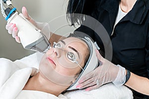 Beauty technician performing skin rejuvenation for removing acne scars, redness and wrinkles on a female patient wearing