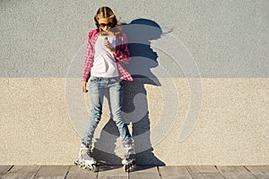 Beauty teen model girl has a chocolate bar, shod in rollers, takes chocolate, on gray wall background.