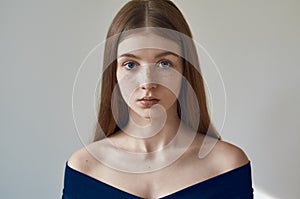 Beauty theme: portrait of a beautiful young girl with freckles on her face and wearing a blue dress on a white background in