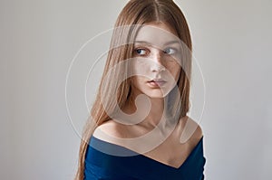 Beauty theme: portrait of a beautiful young girl with freckles on her face and wearing a blue dress on a white background in