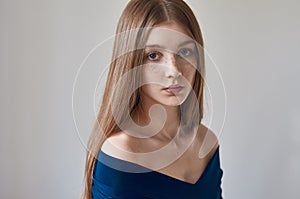 Beauty theme: portrait of a beautiful young girl with freckles on her face and wearing a blue dress on a white background in