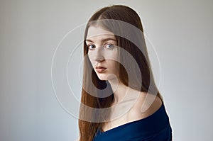 Beauty theme: portrait of a beautiful young girl with freckles on her face and wearing a blue dress on a white background in