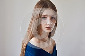 Beauty theme: portrait of a beautiful young girl with freckles on her face and wearing a blue dress on a white background in