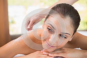 Beauty therapist pouring salt scrub on smiling womans back