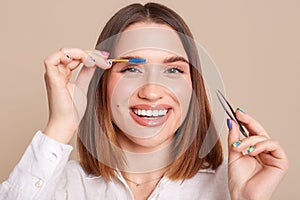 Beauty Tools. Closeup of smiling woman with professional perfect makeup, holding tweezers, plucking brows hair. Metal forceps for