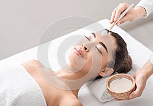 Beauty Treatment. Beautician applying clay mask to Asian woman at spa salon
