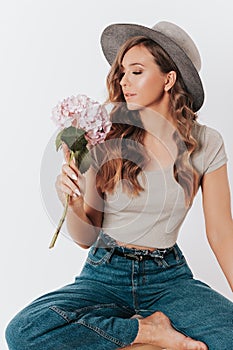 Beauty and trendy young woman in casual clothes posing in studio with hydrangea flowers