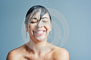 Beauty, water splash and face of woman shower on blue background for wellness, cleaning and grooming. Skincare, bathroom