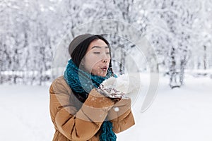 Beauty Winter Asian Girl Blowing Snow in frosty winter Park. Outdoors. Flying Snowflakes