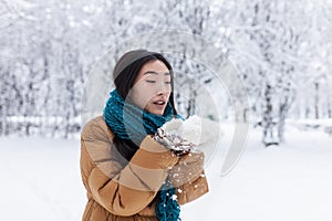 Beauty Winter Asian Girl Blowing Snow in frosty winter Park. Outdoors. Flying Snowflakes