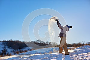 Beauty Winter Girl Blowing Snow in frosty winter Park. Outdoors. Flying Snowflakes. Sunny day. Backlit. Beauty young woman Having