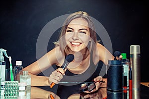 Beauty woman applying makeup. Beautiful girl looking in the mirror and applying cosmetic with a big brush.