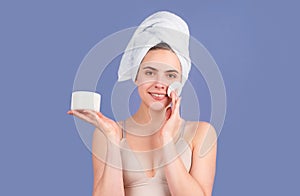 Beauty woman. Cosmetic cream on woman face with clean soft skin. Body care. Woman with towel applying cream on skin