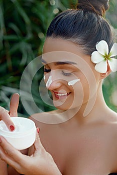 Beauty Woman Face Skin Care. Portrait Of Attractive Young Female Applying Cream And Holding Bottle