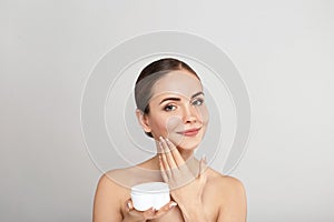 Beauty Woman Face Skin Care. Portrait Of Attractive Young Female Applying Cream  And Holding Bottle.