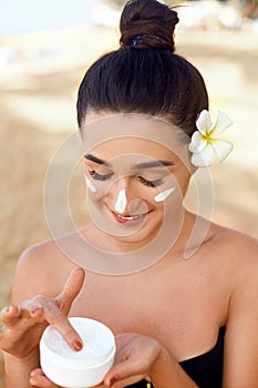 Beauty Woman Face Skin Care. Portrait Of Attractive Young Female Applying Cream And Holding Bottle. Closeup Of Smiling Girl With N