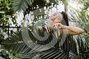 Beauty woman face, tropical plants. Portrait of beautiful Asian mixed raced girl model with dark ponytail hair, natural