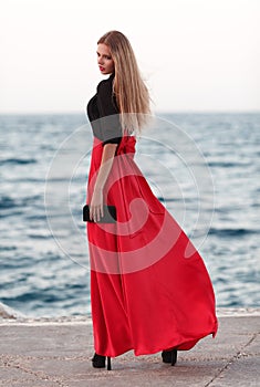 beauty woman in fluttering red dress at the coast. Fashion woman