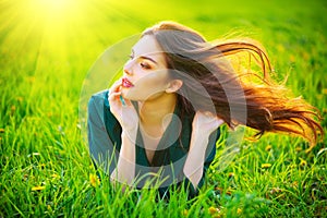 Beauty woman lying on the field enjoying nature. Beautiful brunette girl with healthy long flying hair