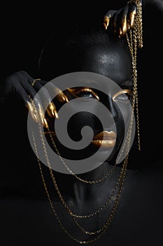 Beauty woman painted in black skin color body art, gold chain in his hands and around his neck. Gold makeup lips eyelids,