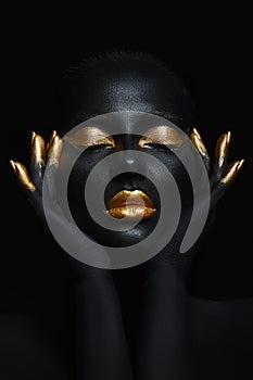 Beauty woman painted in black skin color body art, gold makeup lips eyelids, fingertips nails in gold color paint. Professional