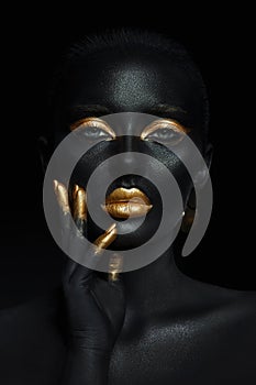 Beauty woman painted in black skin color body art, gold makeup lips eyelids, fingertips nails in gold color paint. Professional