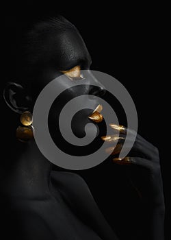 Beauty woman painted in black skin color body art, gold makeup lips eyelids, fingertips nails in gold color paint. Professional
