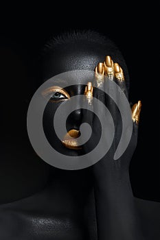 Beauty woman painted in black skin color body art, gold makeup lips eyelids, fingertips nails in gold color paint. Professional