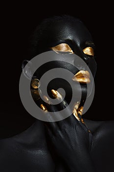 Beauty woman painted in black skin color body art, gold makeup lips eyelids, fingertips nails in gold color paint. Professional