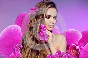 Beauty woman portrait with makeup and long curly hair style with orchid flowers over purple background. Wellness. Smell. Art Photo