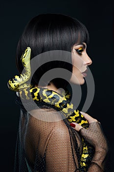 Beauty woman short haircut python yellow snake on her neck. A yellow snake on the shoulders of a girl. Beauty yellow eye shadow