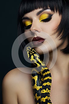 Beauty woman short haircut python yellow snake on her neck. A yellow snake on the shoulders of a girl. Beauty yellow eye shadow